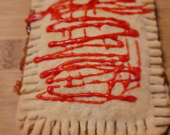 May include: A square pastry with a flaky crust and a red glaze drizzled on top.