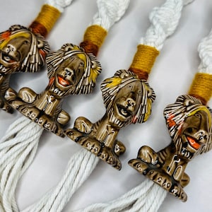 May include: Four ceramic lion figurines with orange, yellow, and brown paint, each attached to a white macrame tassel. The tassels are made of thick, white cotton cord.