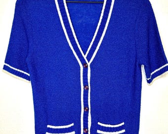 May include: A blue short-sleeved cardigan with white trim around the neckline, cuffs, and pockets. The cardigan has a button-up front.