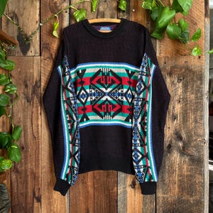 May include: Black sweater with a geometric pattern in red, turquoise, white, and blue. The sweater has a crew neck and long sleeves. The design is centered on the chest and repeated on the sleeves.