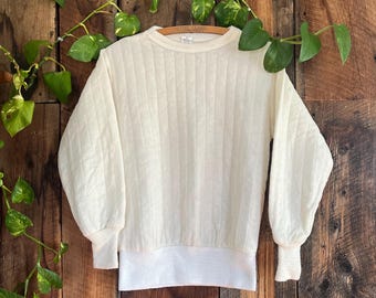 May include: White quilted sweatshirt with long sleeves and a ribbed crew neck. The sweatshirt has a white ribbed band at the bottom.