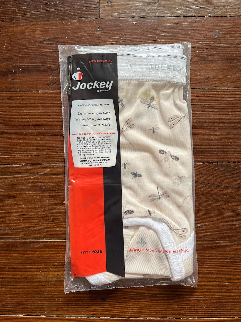 Op de afbeelding: Verzegeld pakket Jockey-ondergoed. Het ondergoed is beige met een libellenpatroon. De verpakking bevat het Jockey-logo en de tekst "Exclusive no-gap front" en "Soft, smooth fabric."