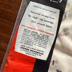 Op de afbeelding: Een verpakking van Jockey-ondergoed. De verpakking is zwart, rood en wit, met de tekst 'Jockey' en 'additional comfort features'. Het label benadrukt kenmerken zoals een naadloze voorkant en zachte stof. Gemaakt in de VS.