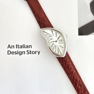 May include: A silver-toned wristwatch with a white face and black Roman numerals. The watch has a unique, curved shape and a brown, textured leather band. The text "An Italian Design Story" is displayed on the left.