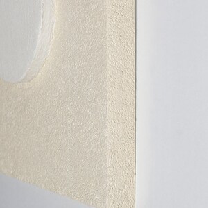 May include: A close-up of a white, textured, square canvas with a white circle in the top left corner.
