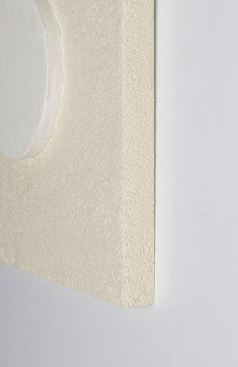 May include: A close-up of a white, textured, square canvas with a white circle in the top left corner.