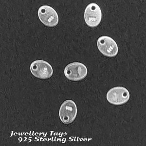 May include: Seven silver oval-shaped jewelry tags with a hole at the top. The tags are on a black background. The text "Jewellery Tags 925 Sterling Silver" is at the bottom of the image.