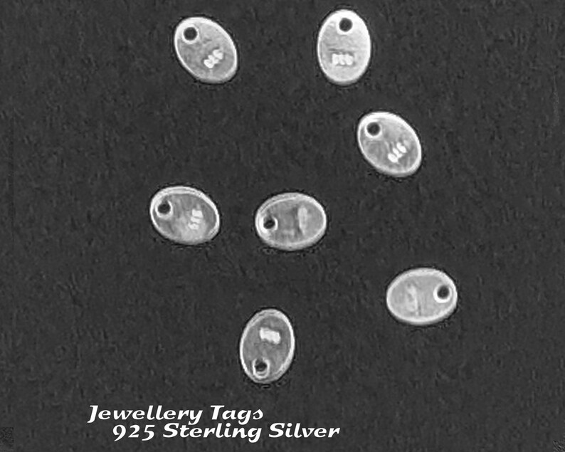 May include: Seven silver oval-shaped jewelry tags with a hole at the top. The tags are on a black background. The text "Jewellery Tags 925 Sterling Silver" is at the bottom of the image.