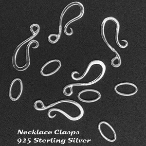 May include: A close-up of ten silver necklace clasps on a black background. The clasps are in various shapes, including oval and swirl designs. The text "Necklace Clasps 925 Sterling Silver" is printed below the clasps.