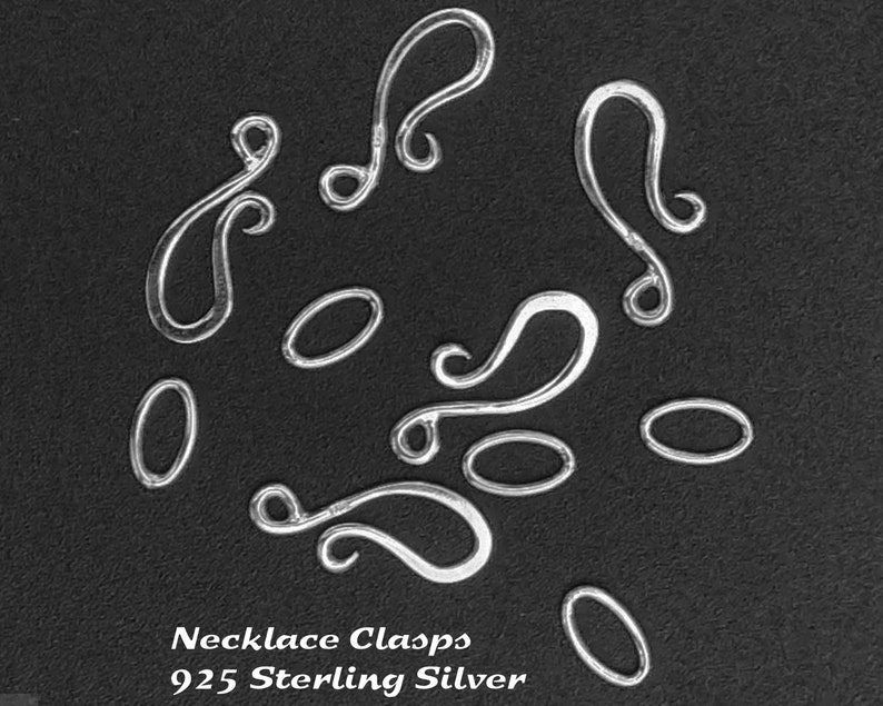 May include: A close-up of ten silver necklace clasps on a black background. The clasps are in various shapes, including oval and swirl designs. The text "Necklace Clasps 925 Sterling Silver" is printed below the clasps.