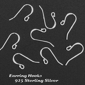 May include: Nine silver earring hooks made of 925 sterling silver. The hooks are arranged in a circle on a black background.