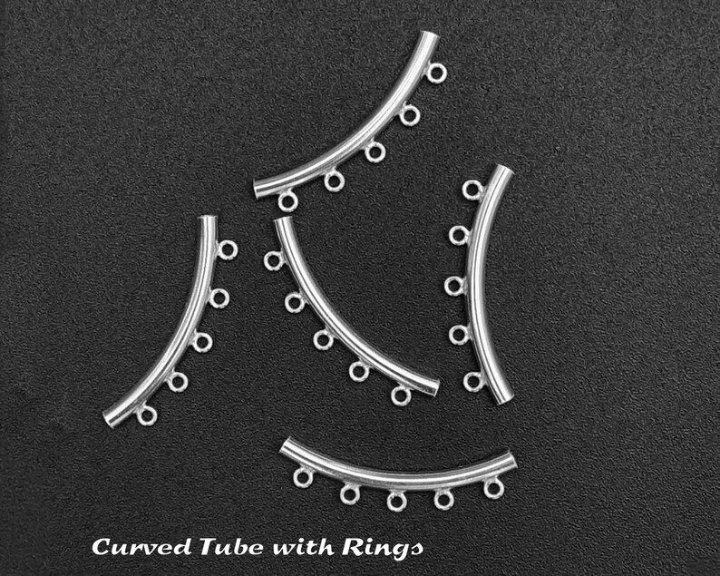May include: Five silver curved tubes with rings. Each tube has five rings attached to it. The tubes are arranged in a semi-circle shape. The background is black. Curved Tube with Rings.