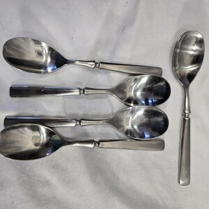 May include: Five silver spoons with rounded bowls and simple handles. The spoons are arranged in a row, with the handles pointing to the right.