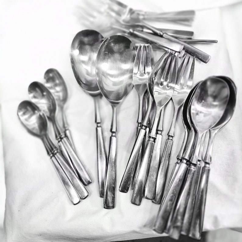 May include: A collection of silver spoons and forks arranged on a white surface. The utensils are all polished and shiny, reflecting the light.