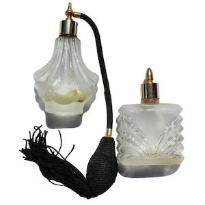 May include: Two vintage perfume bottles. One is a clear, fluted glass bottle with a gold-coloured top and a black atomizer bulb. The other is a frosted glass bottle with a gold-coloured top. Both bottles are empty.