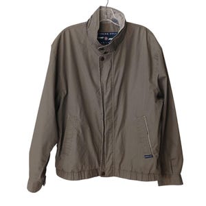 May include: A tan Members Only jacket with a stand-up collar, two front pockets, and a button closure. The jacket has a ribbed hem and cuffs. The brand name is visible on the chest and collar.