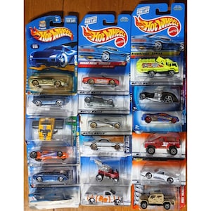 May include: A collection of Hot Wheels toy cars in their original packaging. The cars are various colors, including blue, red, yellow, and silver. The packaging features the Hot Wheels logo and the words "Guaranteed for Life."