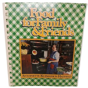 May include: A spiral-bound cookbook titled "Food for Family & Friends" with a green and white checkered cover. The cover features a photo of a woman cooking. The author's name, Antoinette Kuzmanich Hatfield, is printed at the bottom.