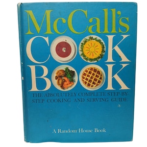 Puede incluir: Un libro de cocina vintage titulado "McCall's COOK BOOK" con una cubierta azul brillante. El título está en letras blancas grandes con acentos amarillos. La portada presenta imágenes de varios platos. El libro es una publicación de Random House.