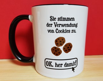 Könnte beinhalten: Weiße Keramiktasse mit schwarzem Henkel. Die Tasse hat einen schwarzen Rand und eine Grafik mit dem Text "Sie stimmen der Verwendung von Cookies zu. OK, her damit!" mit einem Cartoon-Mauszeiger. Auf der Tasse befinden sich drei Schokoladenkekse.