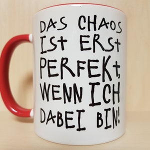 May include: White ceramic mug with a red handle. The mug has black handwritten text that reads "Das Chaos ist erst perfekt, wenn ich dabei bin!"