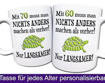 May include: Two white coffee mugs with black text and a green turtle illustration. The text on the mugs reads "Mit 70 muss man NICHTS ANDERS machen als vorher! Nur LANGSAMER!" and "Mit 60 muss man NICHTS ANDERS machen als vorher! Nur LANGSAMER!"