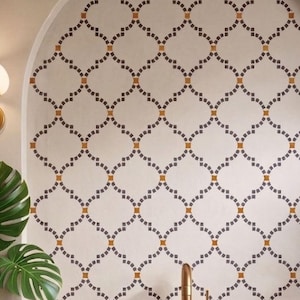 May include: A white oval vessel sink sits on a white marble countertop with a wooden vanity base. Behind the sink is an arched wall niche featuring a cream-colored tile pattern with dark gray and orange accents, flanked by two wall sconces.