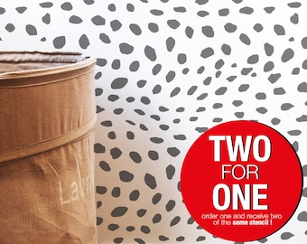 May include: A white wall with a gray dalmatian spot pattern. A brown laundry basket is in the lower left corner. A red circle with the text "TWO FOR ONE" and the text "order one and receive two of the same stencil!" is in the lower right corner.