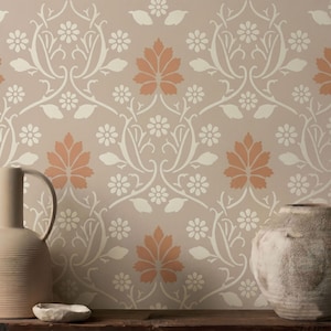May include: A tall, smooth, light beige ceramic vase with a handle and a textured, round, light gray stone vessel. The background features wallpaper with a repeating pattern of white flowers and orange leaves on a light beige surface.