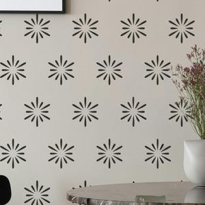 May include: A light beige wall featuring a repeating pattern of black starburst or sunburst motifs. Each motif consists of a central point with twelve radiating petals arranged in a symmetrical circular formation across the surface.