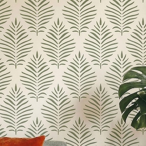 May include: Wallpaper featuring a repeating pattern of olive green fern-like leaf motifs arranged in a vertical diamond grid on a cream-colored background. A portion of a large, dark green monstera leaf is visible in the lower right corner.