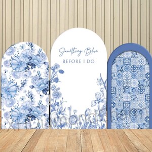 May include: Three blue and white arch-shaped backdrops for a wedding or bridal shower. The center backdrop has the text "Something Blue Before I Do". The backdrop on the left has a floral pattern and the backdrop on the right has a blue and white tile pattern.