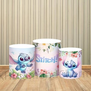Puede incluir: Tres expositores cil&iacute;ndricos con el personaje Stitch de Lilo & Stitch. Los expositores est&aacute;n decorados con motivos florales e ilustraciones de Stitch en varias poses. La palabra "Stitch!" se muestra en un expositor.