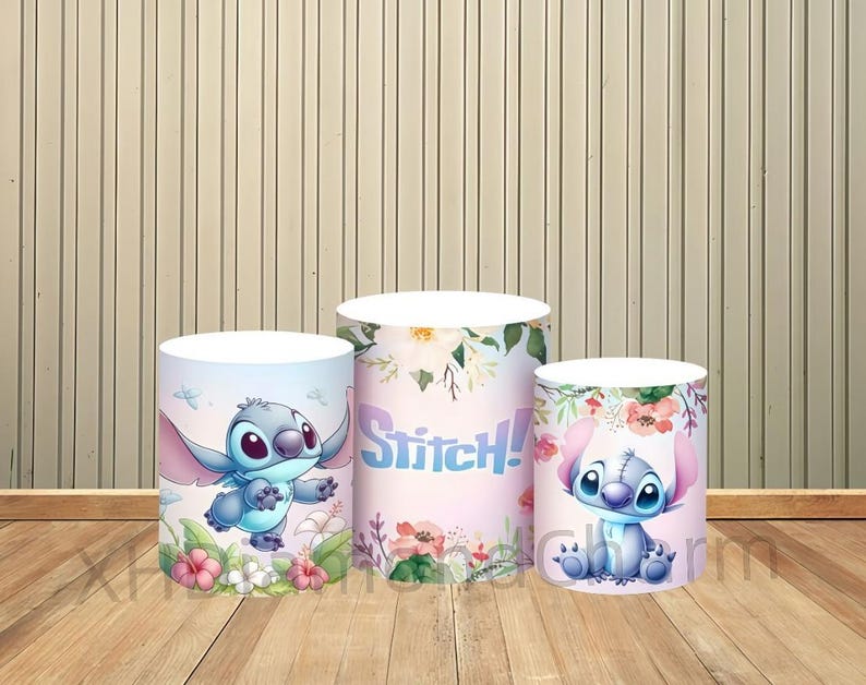 Puede incluir: Tres expositores cil&iacute;ndricos con el personaje Stitch de Lilo & Stitch. Los expositores est&aacute;n decorados con motivos florales e ilustraciones de Stitch en varias poses. La palabra "Stitch!" se muestra en un expositor.