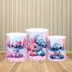 May include: Three cylindrical display stands featuring the cartoon character Stitch and a pink counterpart. The stands have a light pink and blue gradient background with hearts and flowers. The stands are on a wooden surface.