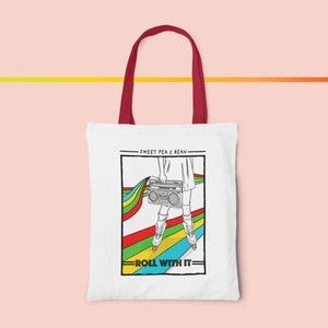 May include: White tote bag with burgundy handles featuring a graphic of a person on roller skates holding a boombox. The design includes a rainbow and the text "Sweet Pea & Bean" and "Roll With It".