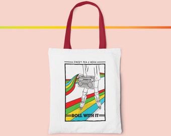 Könnte beinhalten: Weißer Shopper mit weinroten Henkeln. Er zeigt eine Grafik einer Person auf Rollschuhen mit einem Ghettoblaster, mit Regenbogen-Design. Der Text lautet "Sweet Pea & Bean" und "Roll With It".