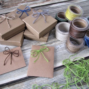 Può includere: Assortimento di scatole regalo e buste in carta kraft marrone con fiocchi di spago in vari colori, tra cui verde, blu e marrone. Ci sono anche bobine di spago in vari colori, tra cui giallo, marrone, verde e blu.