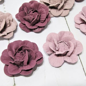 Puede incluir: Una colección de ocho flores de tela de fieltro en tonos rosa y malva. Las flores son todas del mismo tamaño y forma, con un diseño simple y elegante.