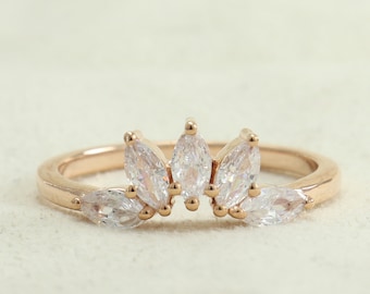 May include: A rose gold ring with a delicate marquise-shaped diamond cluster design. The ring features a row of five marquise-shaped diamonds set in a prong setting, with smaller diamonds set on either side of the center row.