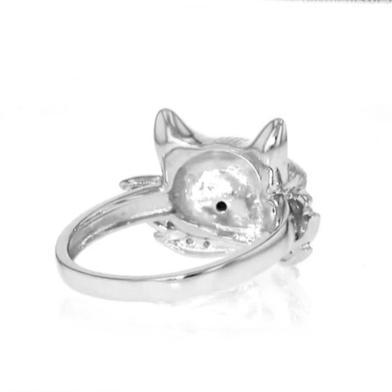 Peut inclure: Une bague en argent avec un motif de t&ecirc;te de chat. La t&ecirc;te du chat est orn&eacute;e de petites pierres et la bague est sertie d'une seule pierre au centre.