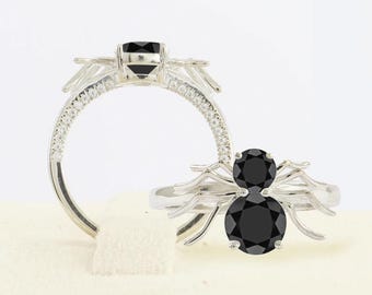 May include: A silver ring with a black spider design. The spider has two large black gemstones for eyes and smaller black gemstones for the body. The ring is set with small clear gemstones around the band.