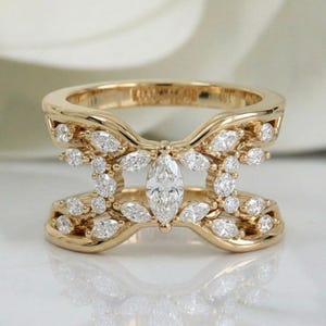 Könnte beinhalten: Ein Goldring mit einem breiten, durchbrochenen Banddesign. Der Ring ist mit zahlreichen kleinen, runden Diamanten im Brillantschliff und einem einzelnen, markanten Diamanten im Marquiseschliff besetzt, der horizontal in der Mitte sitzt.