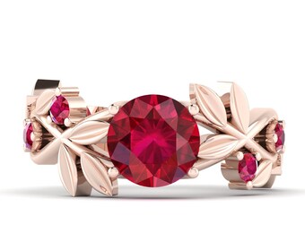 Könnte beinhalten: Roségoldener Ring mit einem großen, runden, rubinroten Edelstein in der Mitte, flankiert von kleineren Rubin-Akzenten. Das Ringband ist mit einem blattartigen Design verziert, das eine elegante, von der Natur inspirierte Ästhetik schafft. Ein wunderschönes Schmuckstück.