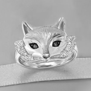 Peut inclure: Une bague en argent avec un motif de t&ecirc;te de renard. Le renard a des yeux noirs et est entour&eacute; de petits diamants.