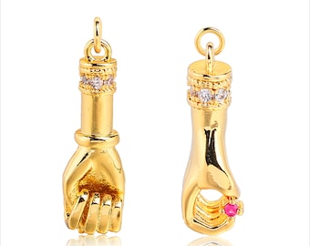 May include: Two gold-tone hand charms with clear and pink crystal accents. The charms are designed to look like a hand with a closed fist and a hand with an open palm.