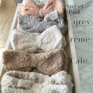 K&ouml;nnte beinhalten: Sechs flauschige Haarb&auml;nder in Schleifenform in einem Holztablett. Die Haarb&auml;nder sind in verschiedenen Farben erh&auml;ltlich, darunter Mint, Sweet Pink, Soft Grey, Cr&egrave;me, Cafe und Toffee. Der Text zeigt die Farbe jedes Stirnbandes an.