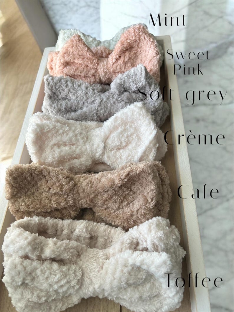 K&ouml;nnte beinhalten: Sechs flauschige Haarb&auml;nder in Schleifenform in einem Holztablett. Die Haarb&auml;nder sind in verschiedenen Farben erh&auml;ltlich, darunter Mint, Sweet Pink, Soft Grey, Cr&egrave;me, Cafe und Toffee. Der Text zeigt die Farbe jedes Stirnbandes an.