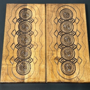May include: Two wooden game boards with intricate carved designs. Each board features a row of five circular patterns with a diamond shape between each circle. The boards are a light brown color with a natural wood grain.