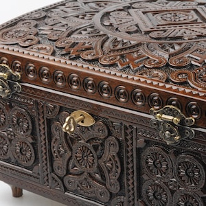 May include: A dark brown wooden box with intricate carvings and brass hinges. The box has a keyhole and a key in the lock. The box is decorated with a floral pattern.